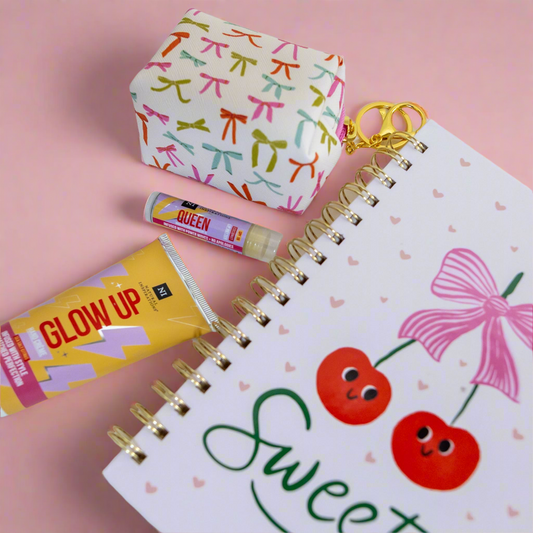 Notebook with cherry and bow design, lip balm, hand cream and small keychain purse on a pink background
