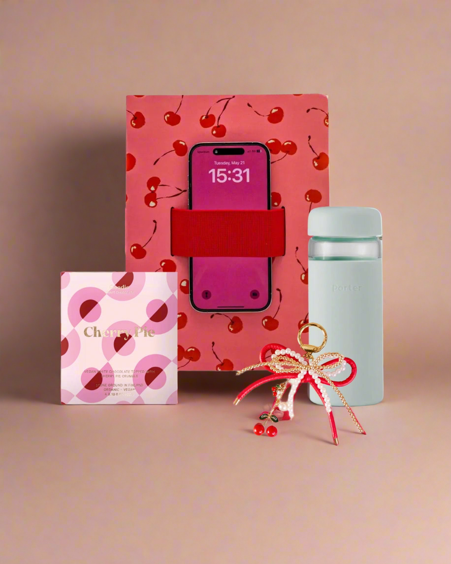 phone loop notebook with cherry design, light blue water bottle, chocolate bar, and small cherry charm keychain on a beige background