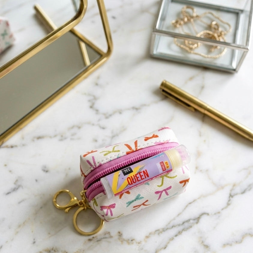 A keychain pouch with a colorful bow print and a pink zipper, featuring a gold key ring clasp with a lip butter balm. The perfect curated gift for celebrations, milestones, graduations, teens, tweens, pre-teens, stationery lovers.
