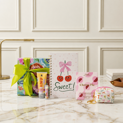 A curated stationery gift set includes a wrapped gift box with a satin ribbon, a heart designed spiral notebook with cherries and the word 'Sweet!', a hand cream, lip butter balm, a salted caramel chocolate bar and and a small bow designed keychain pouch. 

The perfect curated gift for celebrations, milestones, graduations, teens, tweens, pre-teens, stationery lovers.