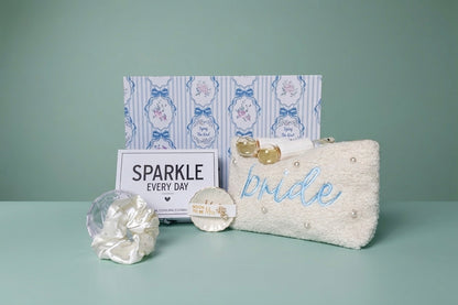 Mrs. Glam bridal gift set with pearl pouch, embroidered with 'bride' in blue and ring dish with crystal earring studs for the "soon to be" Mrs, a white crystal beaded hair scrunchie in a clear crystal diamond case, and a  'SPARKLE EVERY DAY' box that includes a eye cooling globes. Upgraded keepsake gift box. 