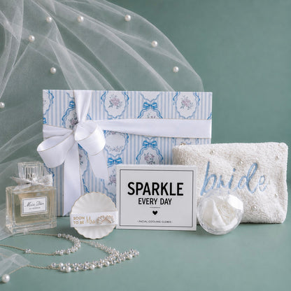 Bride shower curated gift set arranged on a sage green background, featuring a blue and white patterned gift box with a white ribbon, a white embroidered 'bride' pouch, a perfume bottle, pearl jewelry, a facial cooling globes enclosed in a 'SPARKLE EVERY DAY' box. 