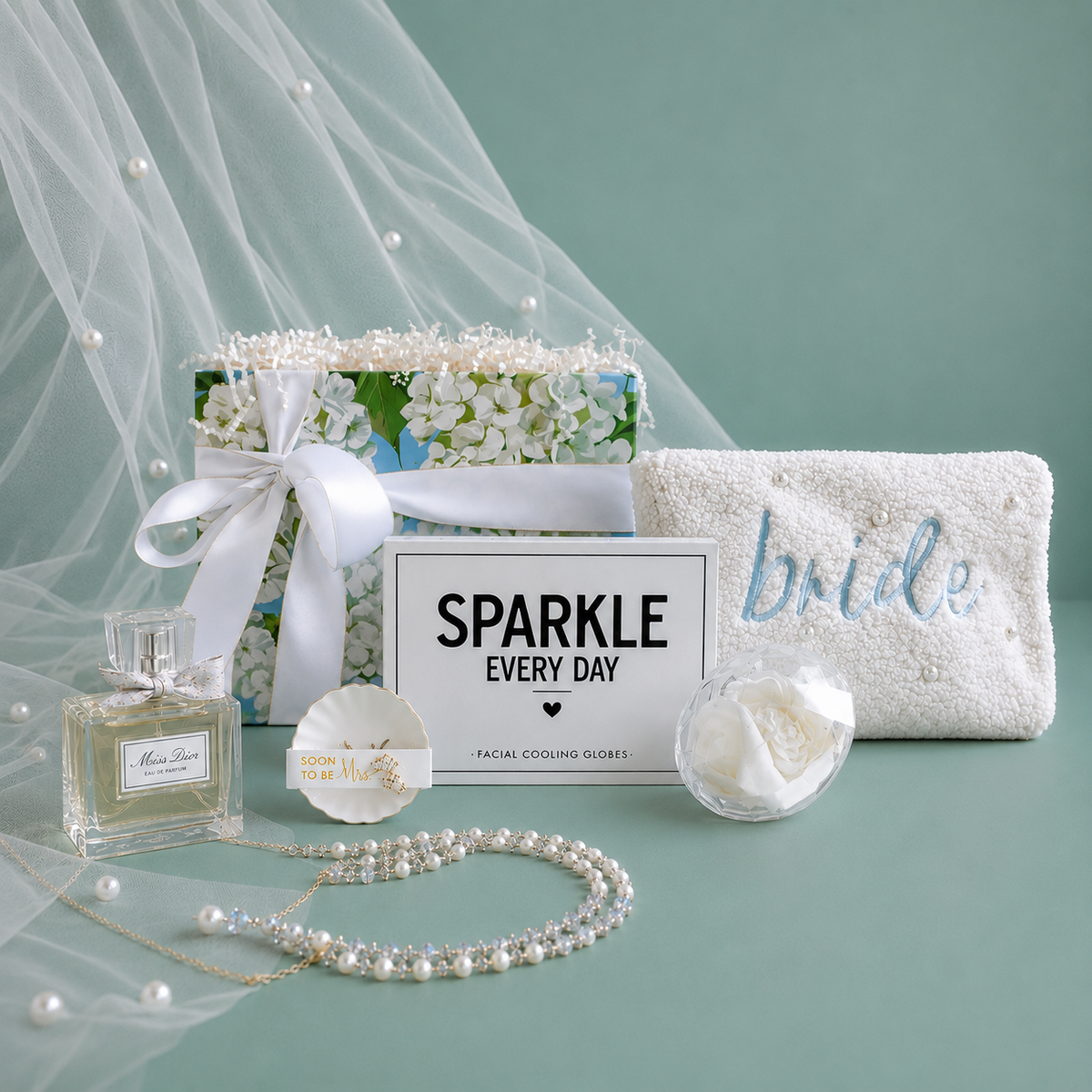 A bridal shower curated gift with pearl pouch, embroidered with 'bride' in blue and ring dish with crystal earring studs for the "soon to be" Mrs, a white crystal beaded hair scrunchie in a clear crystal diamond case, and a facial cooling globes enclosed in 'SPARKLE EVERY DAY' box.