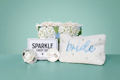 Mrs. Glam bridal gift set with pearl pouch, embroidered with 'bride' in blue and ring dish with crystal earring studs for the "soon to be" Mrs, a white crystal beaded hair scrunchie in a clear crystal diamond case, and a  'SPARKLE EVERY DAY' box that includes a eye cooling globes. 