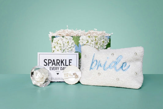 Mrs. Glam bridal gift set with pearl pouch, embroidered with 'bride' in blue and ring dish with crystal earring studs for the "soon to be" Mrs, a white crystal beaded hair scrunchie in a clear crystal diamond case, and a  'SPARKLE EVERY DAY' box that includes a eye cooling globes. 
