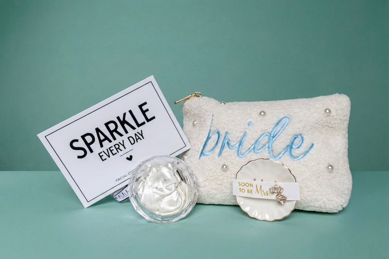 Mrs. Glam bridal gift set with pearl pouch, embroidered with 'bride' in blue and ring dish with crystal earring studs for the "soon to be" Mrs, a white crystal beaded hair scrunchie in a clear crystal diamond case, and a  'SPARKLE EVERY DAY' box that includes a eye cooling globes. 