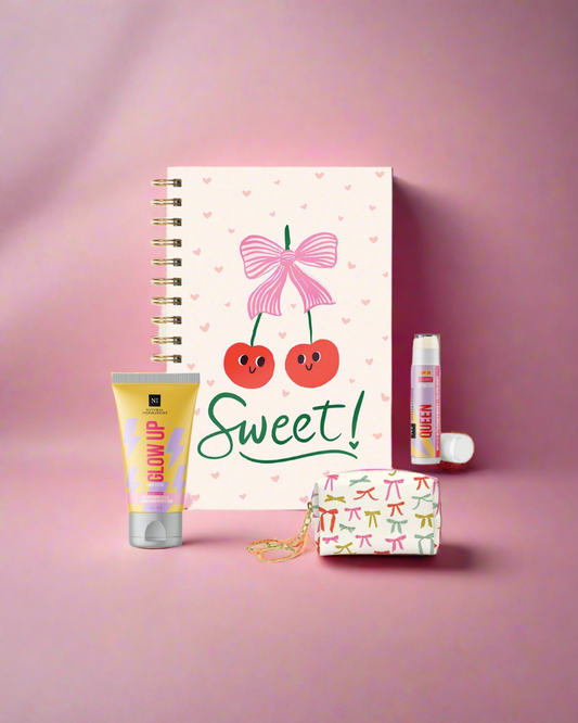 Notebook with cherry and bow design, lip balm, hand creme, and small keychain purse on a pink background