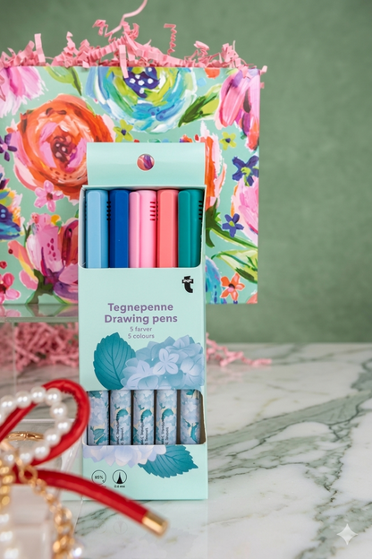Set of writing pens in a colorful box with floral design on a marble surface.